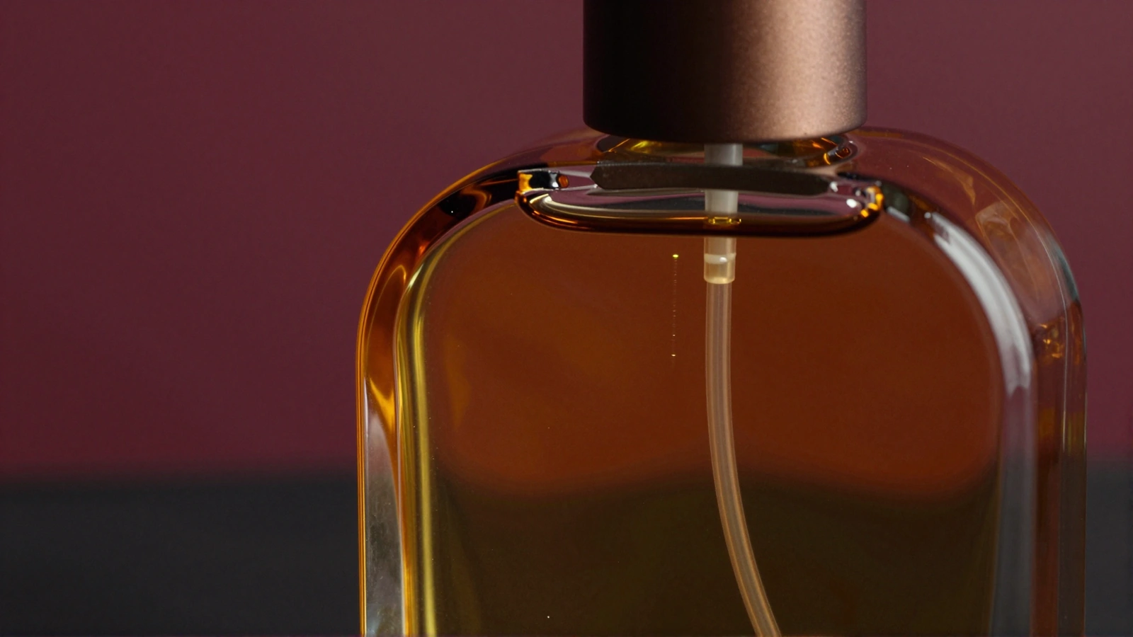 Eigenständige Nahaufnahme von amberfarbenem Flakonglas und einem bronzefarbenen Verschluss vor dunklem Violett.
