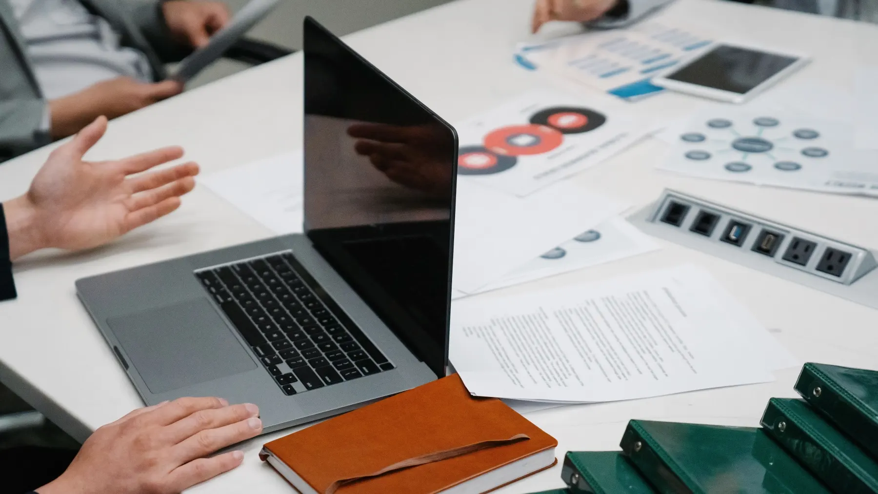 Mehrere Personen besprechen Unterlagen und einen Laptop an einem Arbeitstisch.